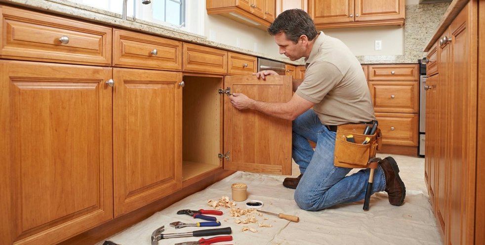 Handyman repairing a kitchen cabinet door hinge in a home kitchen